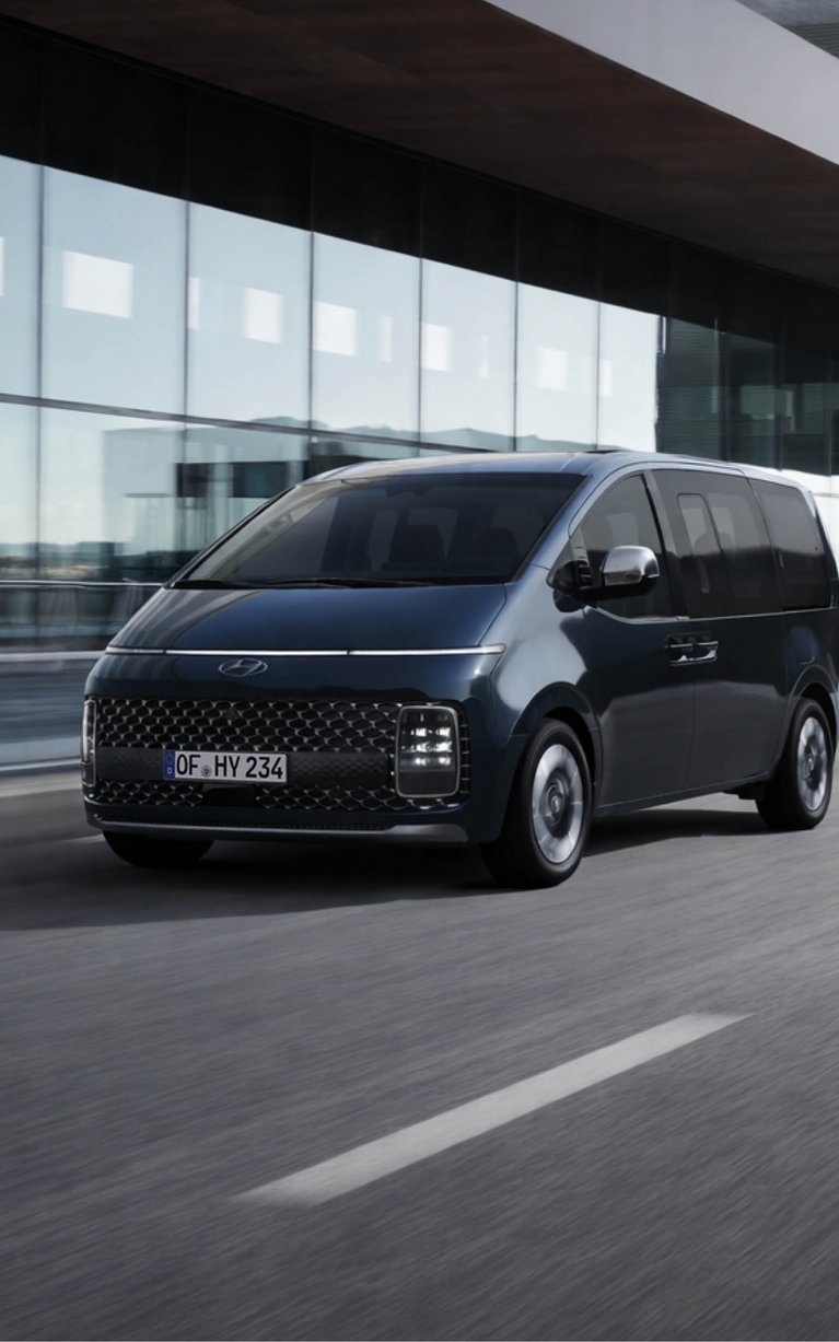 Hyundai STARIA fährt vor moderner Architektur auf der Straße – Leasing Angebot zu günstigen Konditionen bei S&G