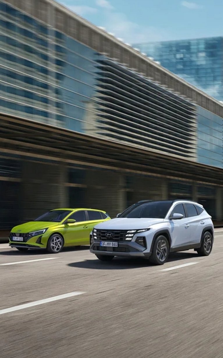 Mehrere Hyundai Neuwagen, darunter i20 und TUCSON, fahren durch eine moderne Stadt – attraktive Hyundai Angebote bei S&G