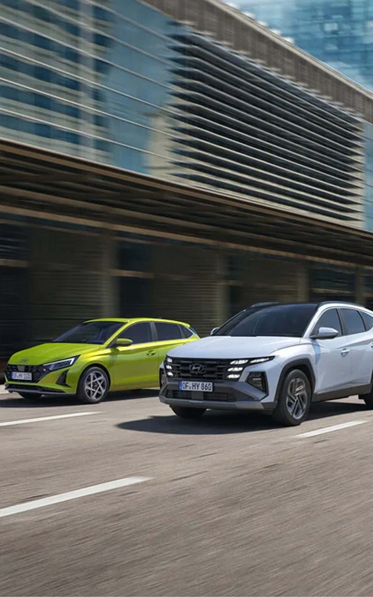 Mehrere Hyundai Neuwagen, darunter i20 und TUCSON, fahren durch eine moderne Stadt – attraktive Hyundai Angebote bei S&G