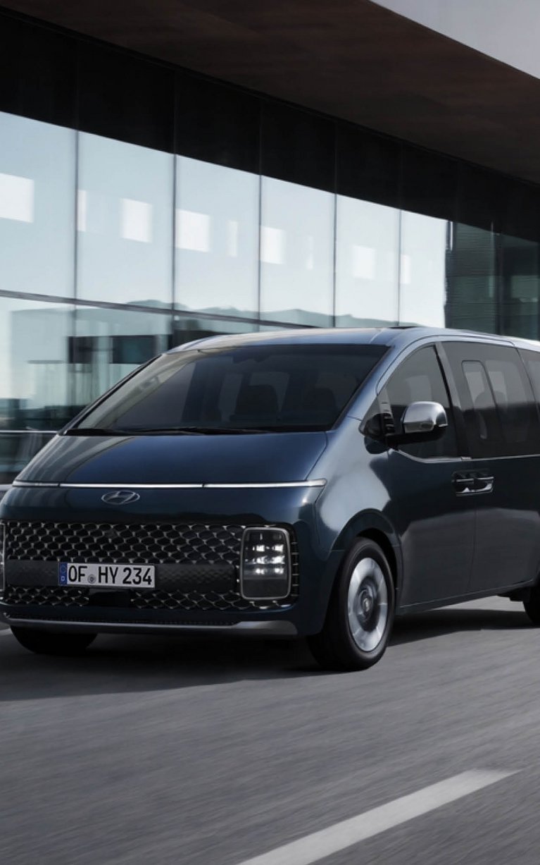 Hyundai STARIA fährt vor moderner Architektur auf der Straße – Leasing Angebot zu günstigen Konditionen bei S&G