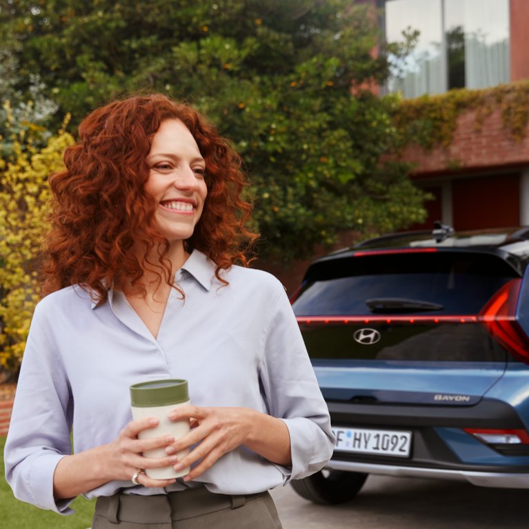 Geschäftsfrau mit Smartphone vor blauem Hyundai auf Einfahrt eines modernen Gebäudes – Symbolbild für Hyundai Angebote für Gewerbekunden bei S&G.