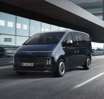 Schwarzer Hyundai STARIA fährt vor moderner Architektur entlang. Promotionbild für sofort verfügbare Fahrzeuge und günstige Finanzierung im Autohaus Zondler.